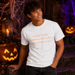 A smiling young man wearing a white graphic t-shirt with orange text that reads 'I couldn't find a costume so this t-shirt will just have to do.' He is posed outdoors on Halloween-themed steps with jack-o'-lanterns and cobwebs in the background.