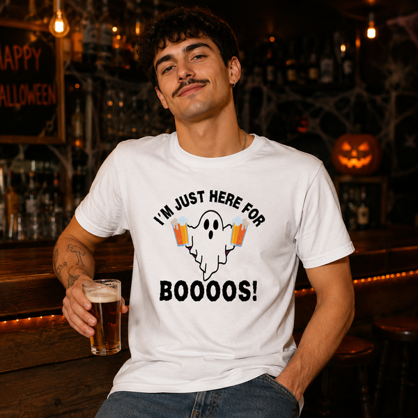 A man wearing a white graphic t-shirt with a Halloween ghost design and the text 'I'M JUST HERE FOR BOOOOS!' while holding a pint of beer in a dimly lit bar setting.