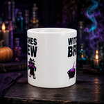 A white ceramic mug with Halloween-themed graphics, including a witch silhouette and a cauldron, displayed on a dark wooden table with candles and potion bottles in the background.